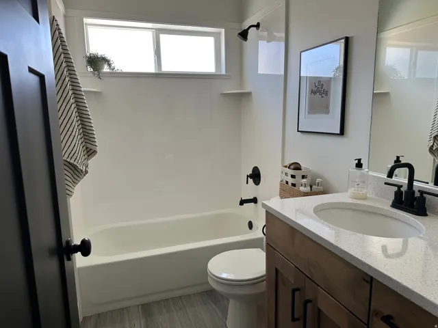 White bathtub with matte black fixtures, a single vanity with stone-finish countertop, and wood-finish cabinetry