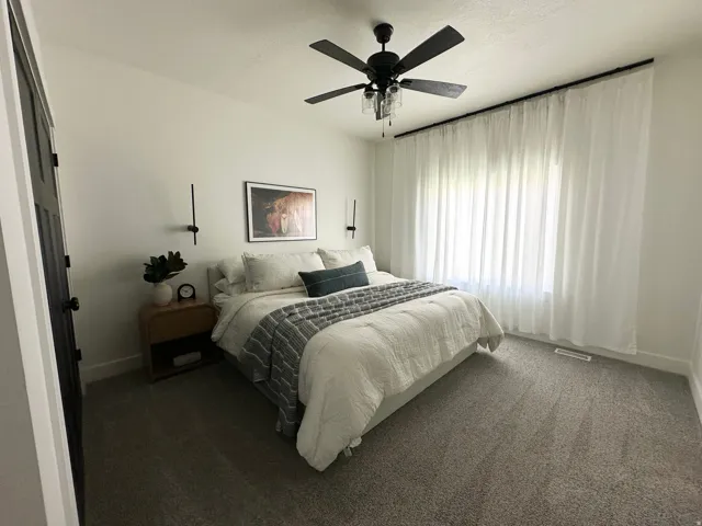 Plush grey carpeting, black ceiling fan with integrated lighting, wall-mounted sconces, and full-wall window treatments