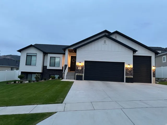 Contemporary split-level residence featuring a white and black exterior, a two-car garage with black doors, and a concrete driveway