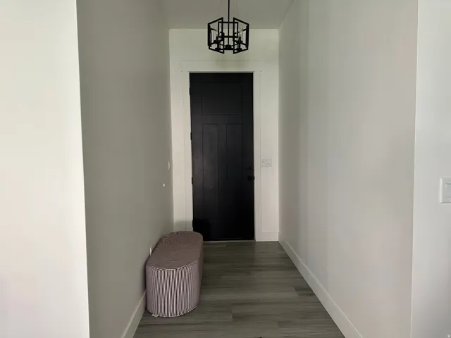 Hallway featuring wood-finish flooring, white walls, and a black entryway door with contrasting white trim