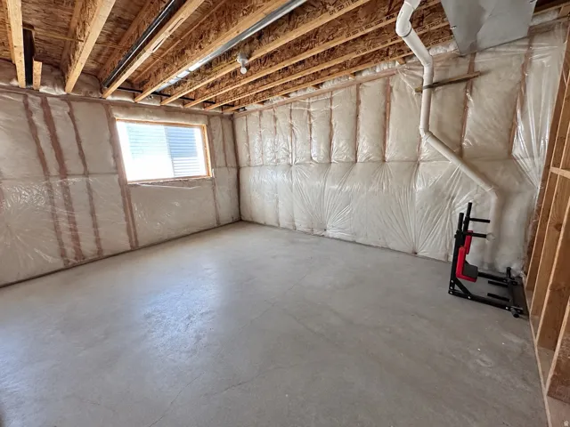 Unfinished basement with concrete flooring, exposed wood joists, and a visible window for natural light