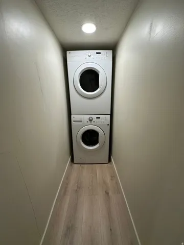 Stacked laundry appliances with wood-finish flooring and recessed lighting
