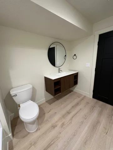 Floating wood-finish vanity with an integrated white sink and a round black-framed mirror