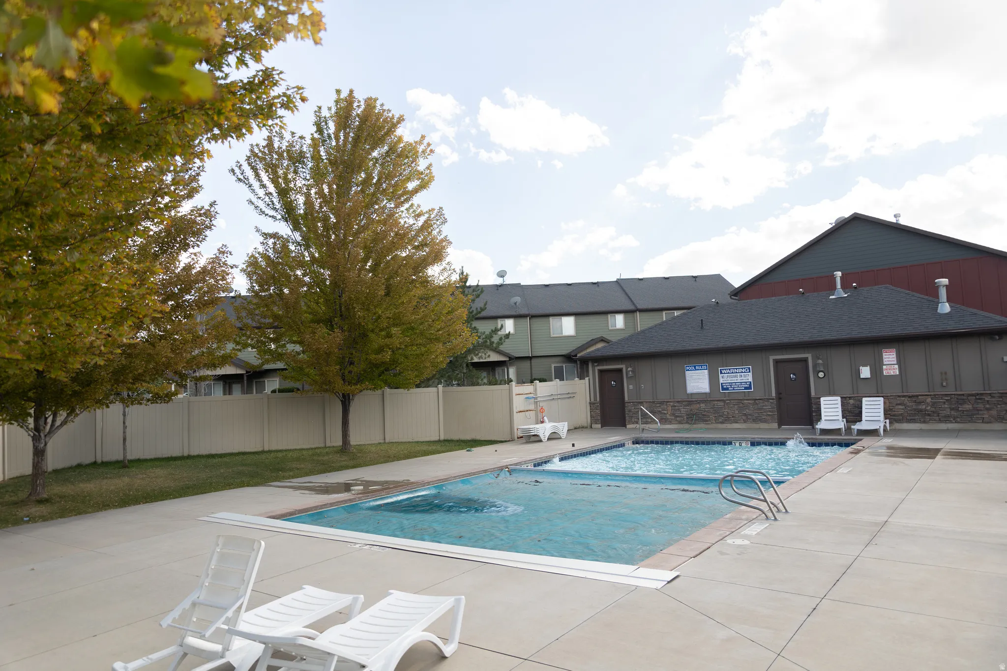Community pool with concrete decking, featuring a separate pool house with dual entry doors