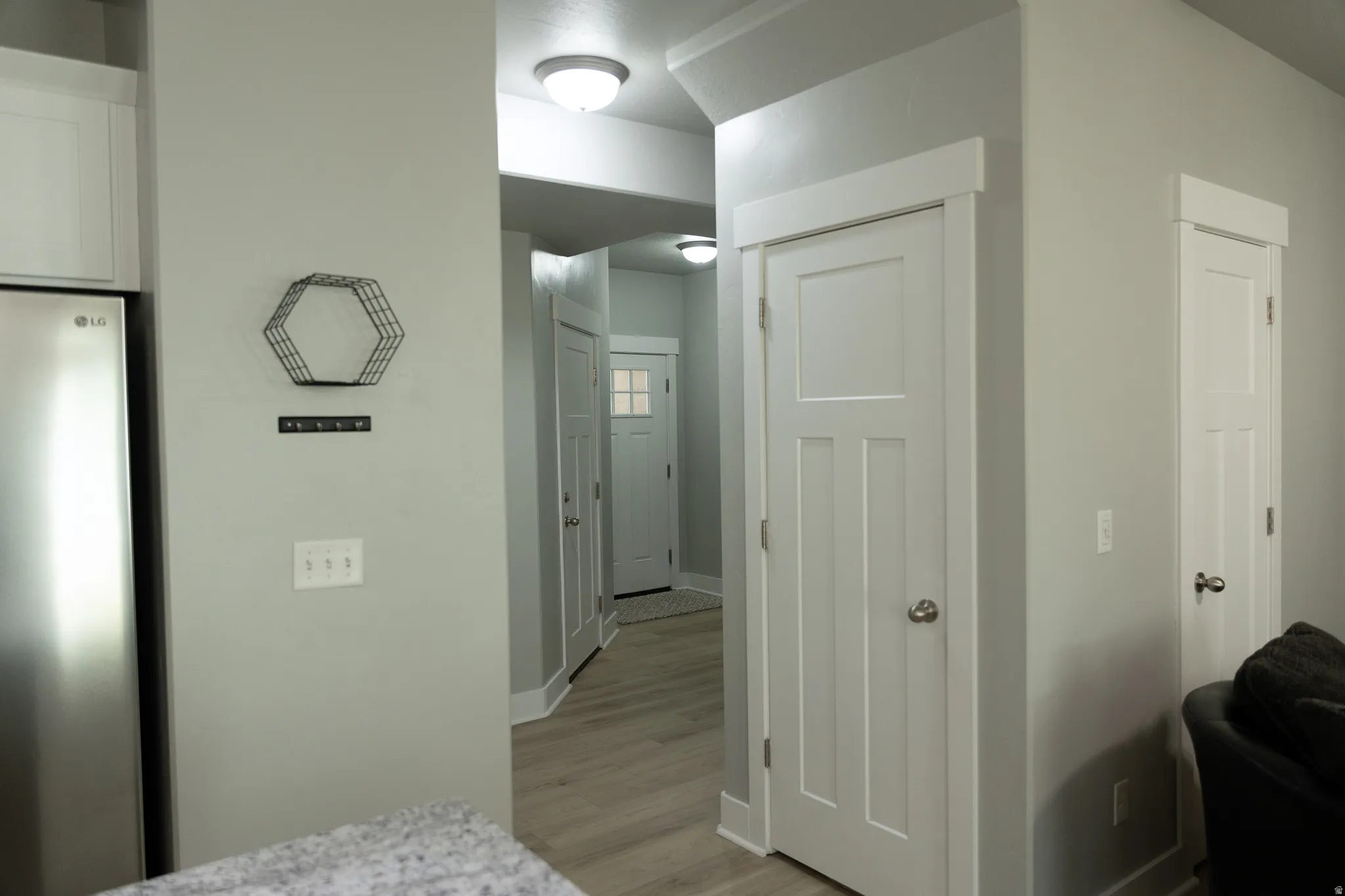 Stainless steel refrigerator, white shaker-style cabinetry, light gray walls, white paneled doors with silver hardware, and wood-finish flooring