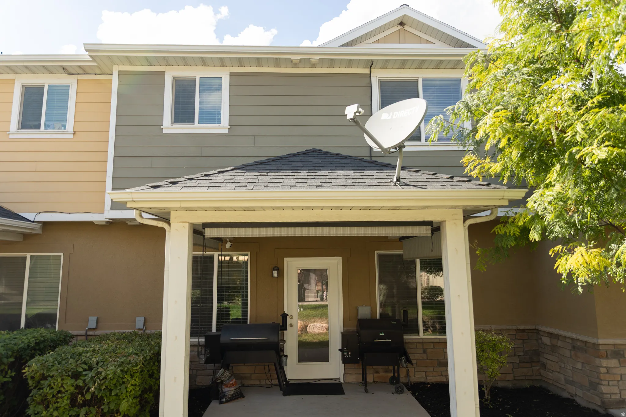 Covered patio entrance with a dark-shingle roof, white trim, and stone veneer accents