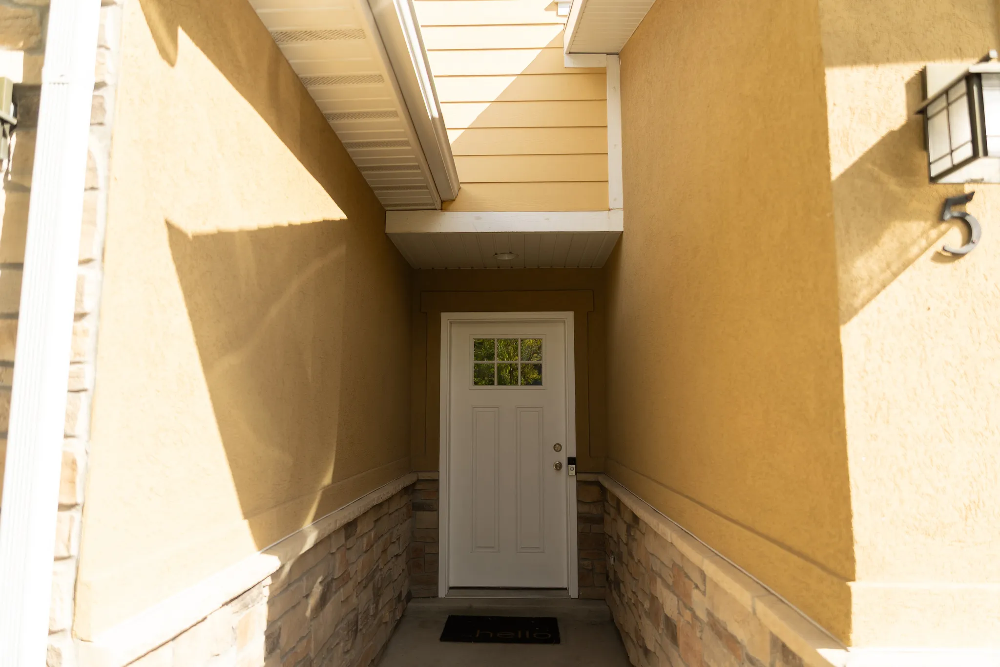 Entryway featuring a white door with divided lites, stucco exterior, stone veneer accents, and an exterior wall lantern