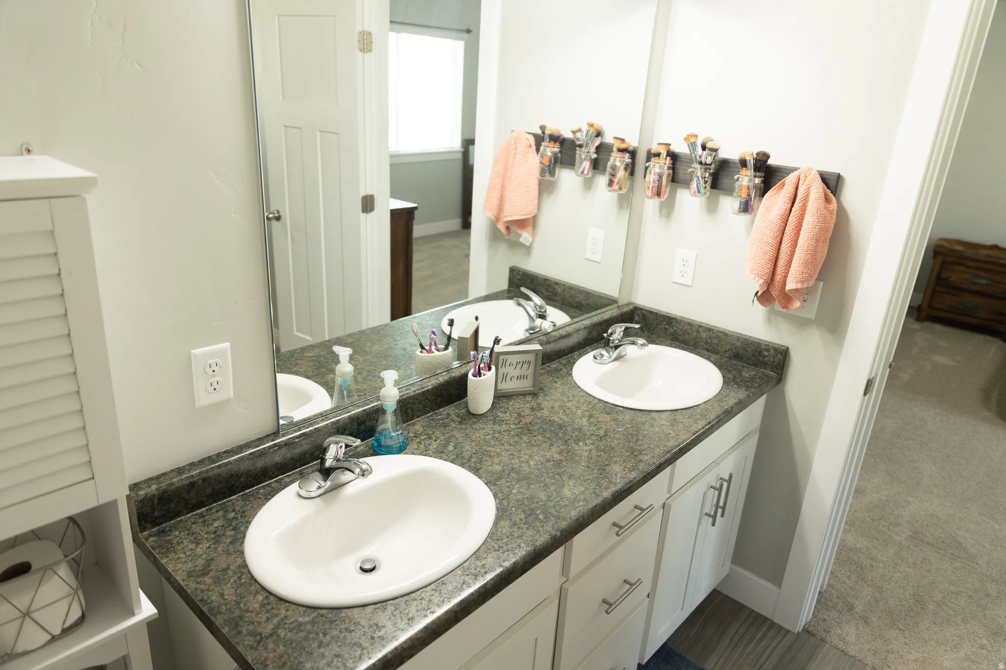 Dual vanity with integrated sinks, dark speckled countertop, white cabinetry with silver-tone hardware, and a framed mirror