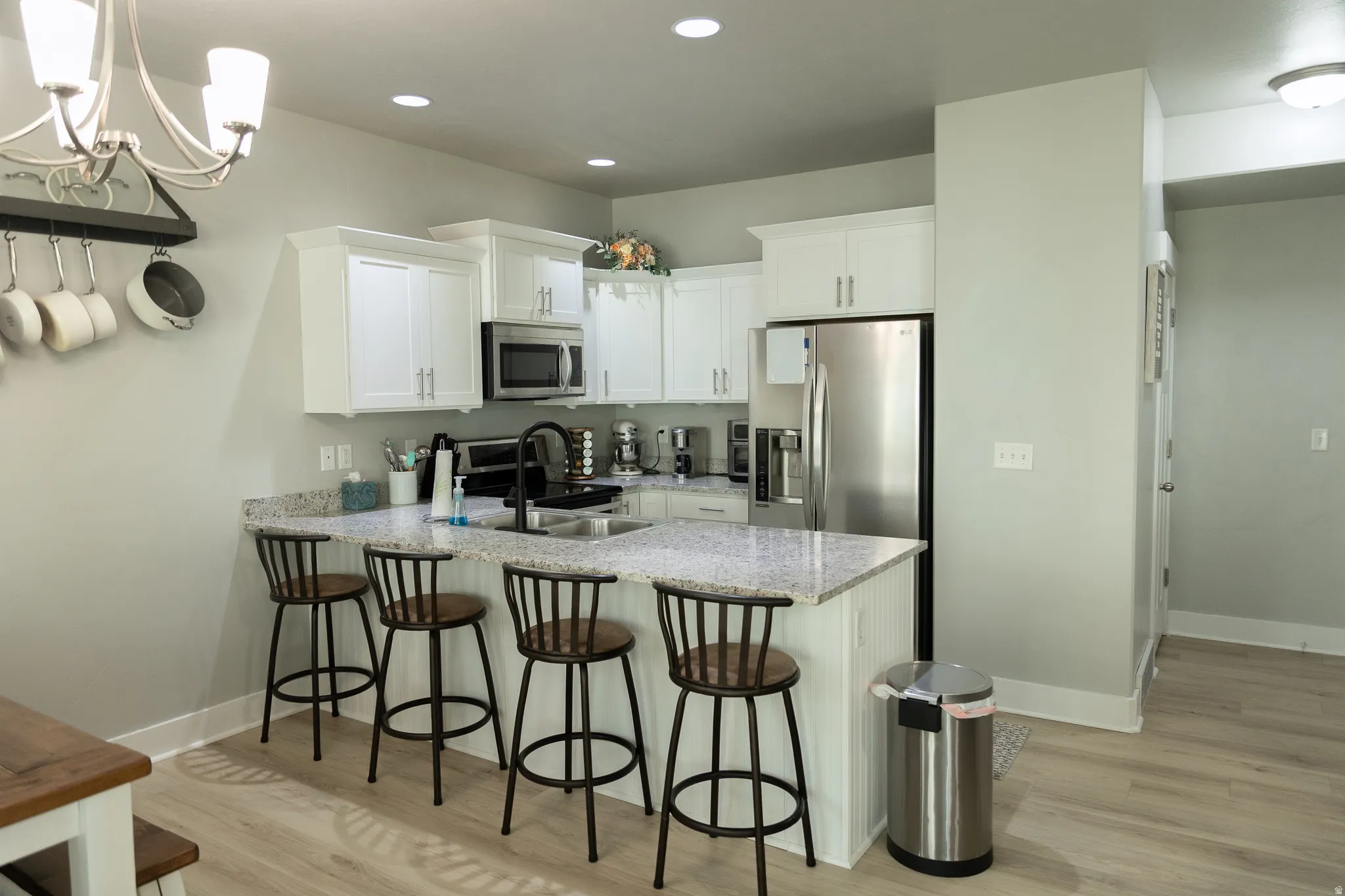 White cabinetry, stainless steel appliances, speckled countertops, recessed lighting, and wood-finish flooring