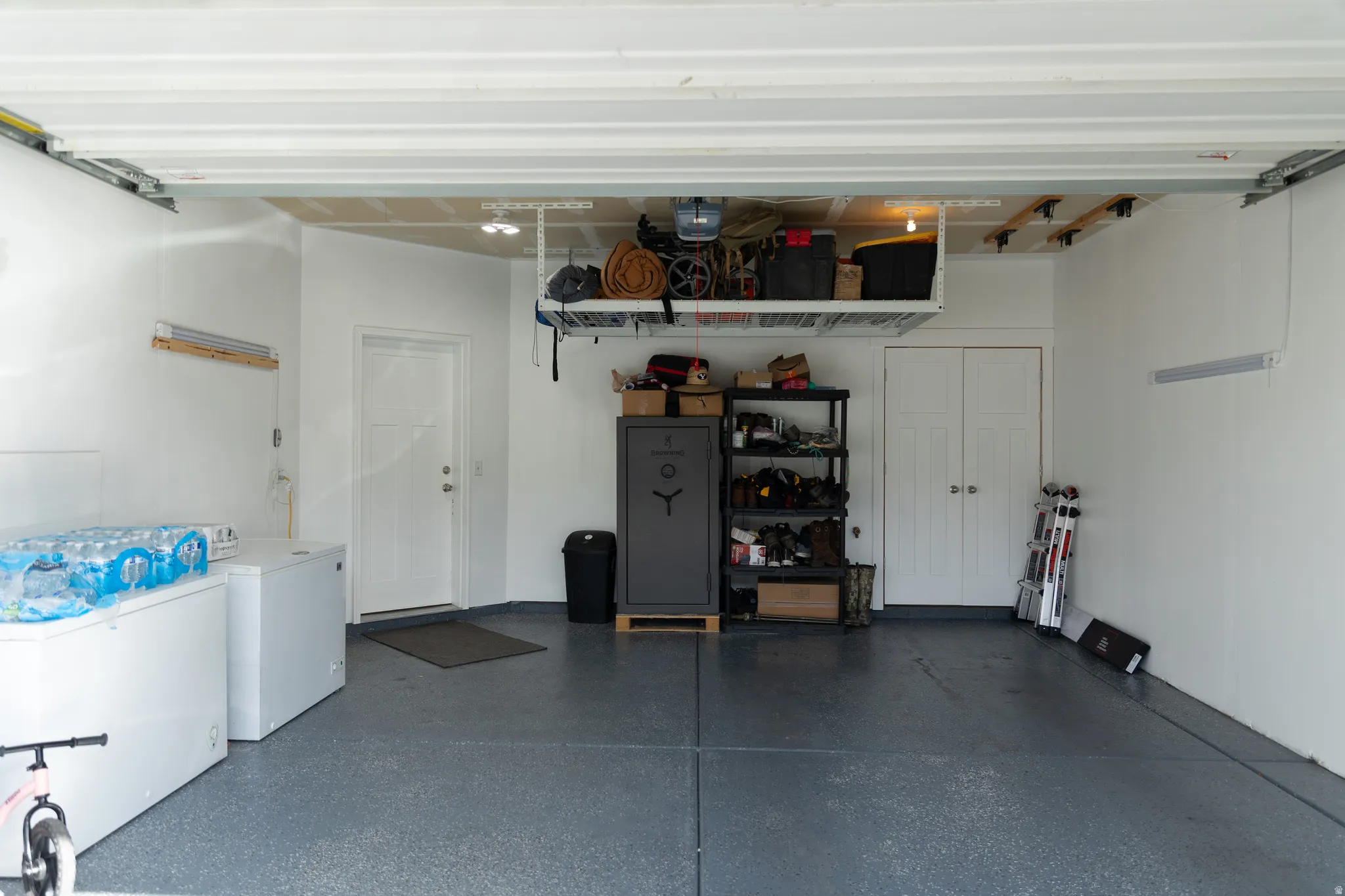 Epoxy-coated flooring, overhead storage racks, interior access door, recessed ceiling lighting, and built-in closet with bifold doors