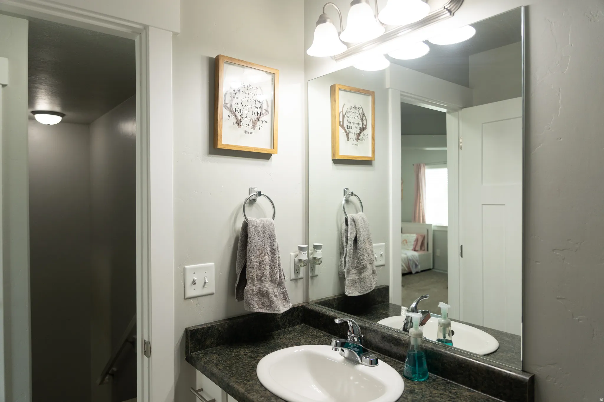 Vanity with a single basin sink, wall-mounted mirror, and overhead light fixture