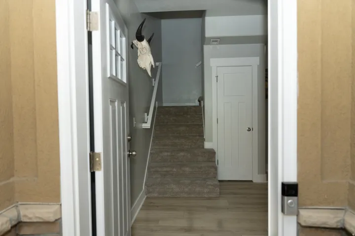 Entryway featuring a white paneled door with window, wood-finish flooring, and carpeted stairs with a handrail