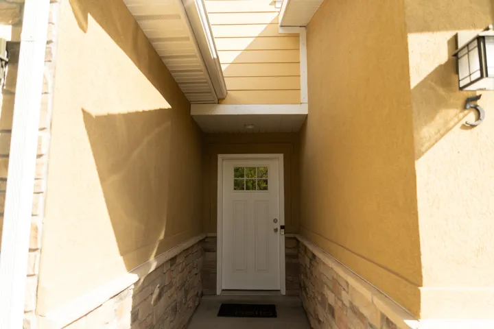 Entryway featuring a white door with divided lites, stucco exterior, stone veneer accents, and an exterior wall lantern