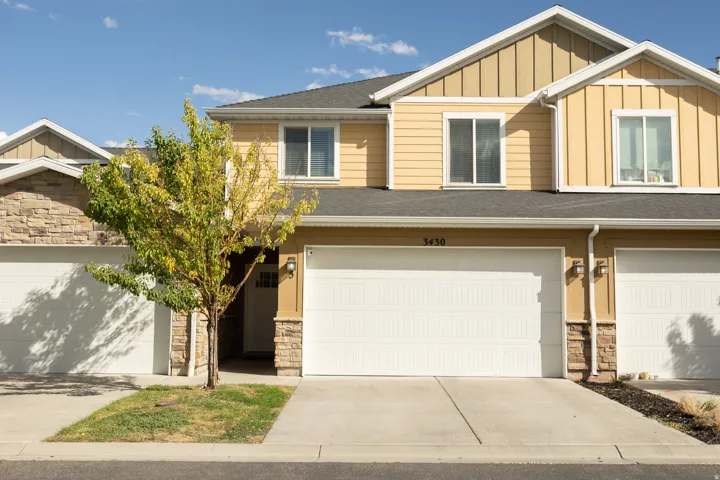 Multi-level property exterior with light yellow siding and stone accents, featuring an attached garage and concrete driveway