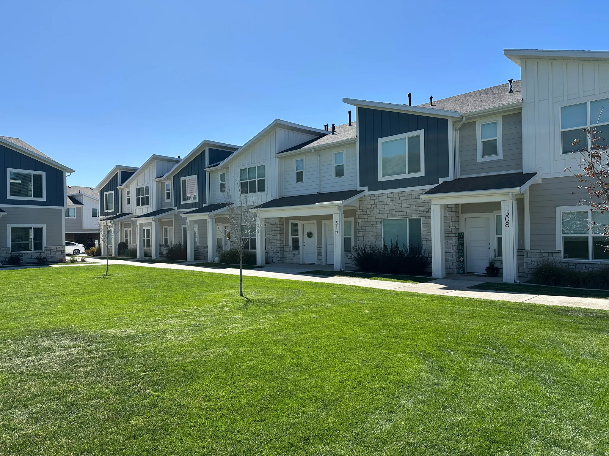 Row of townhomes featuring stone and siding exteriors, covered front porches, and a manicured lawn