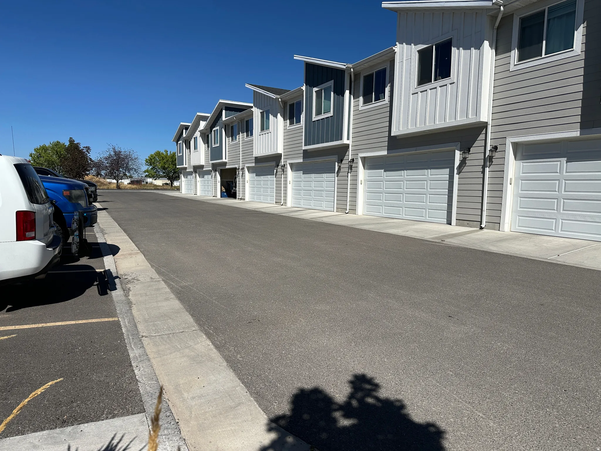Row of multi-level townhomes featuring light gray siding, white vertical accent panels, and individual garage doors
