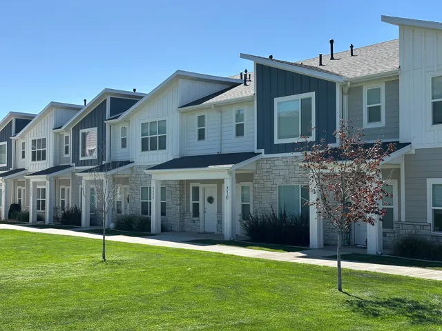 Modern townhomes featuring vertical siding, stone veneer accents, covered entryways, and a pitched roofline