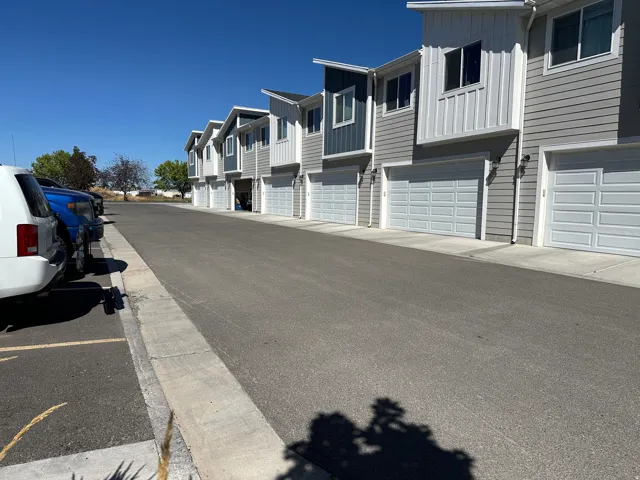 Row of multi-level townhomes featuring light gray siding, white vertical accent panels, and individual garage doors
