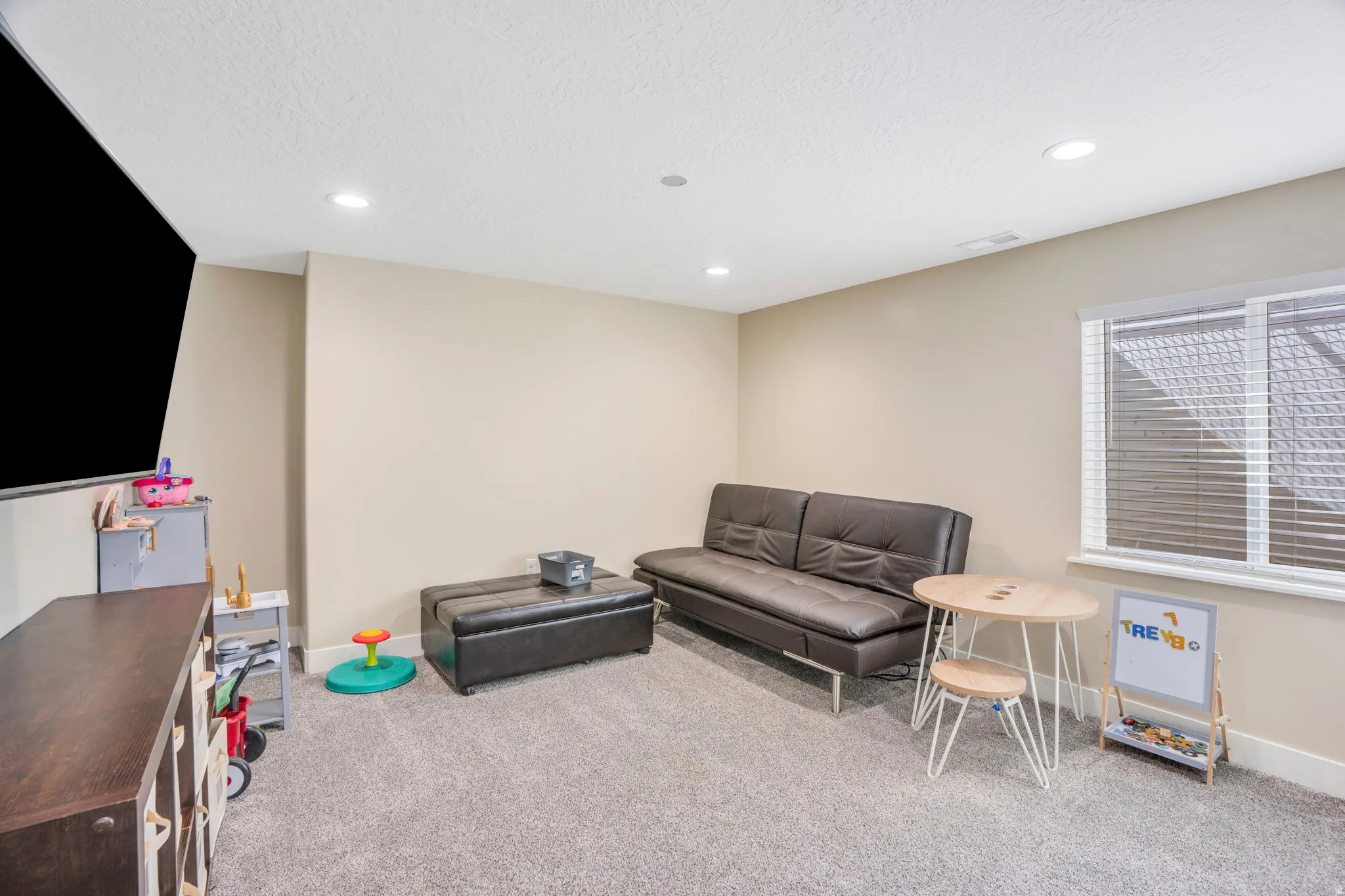 Recessed lighting, neutral wall tones, window with horizontal blinds, carpeted flooring, and a built-in media console