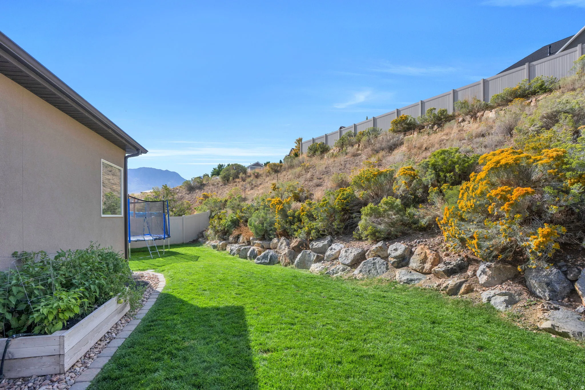Manicured lawn with a retaining rock wall, adjacent to a sloped, natural landscape