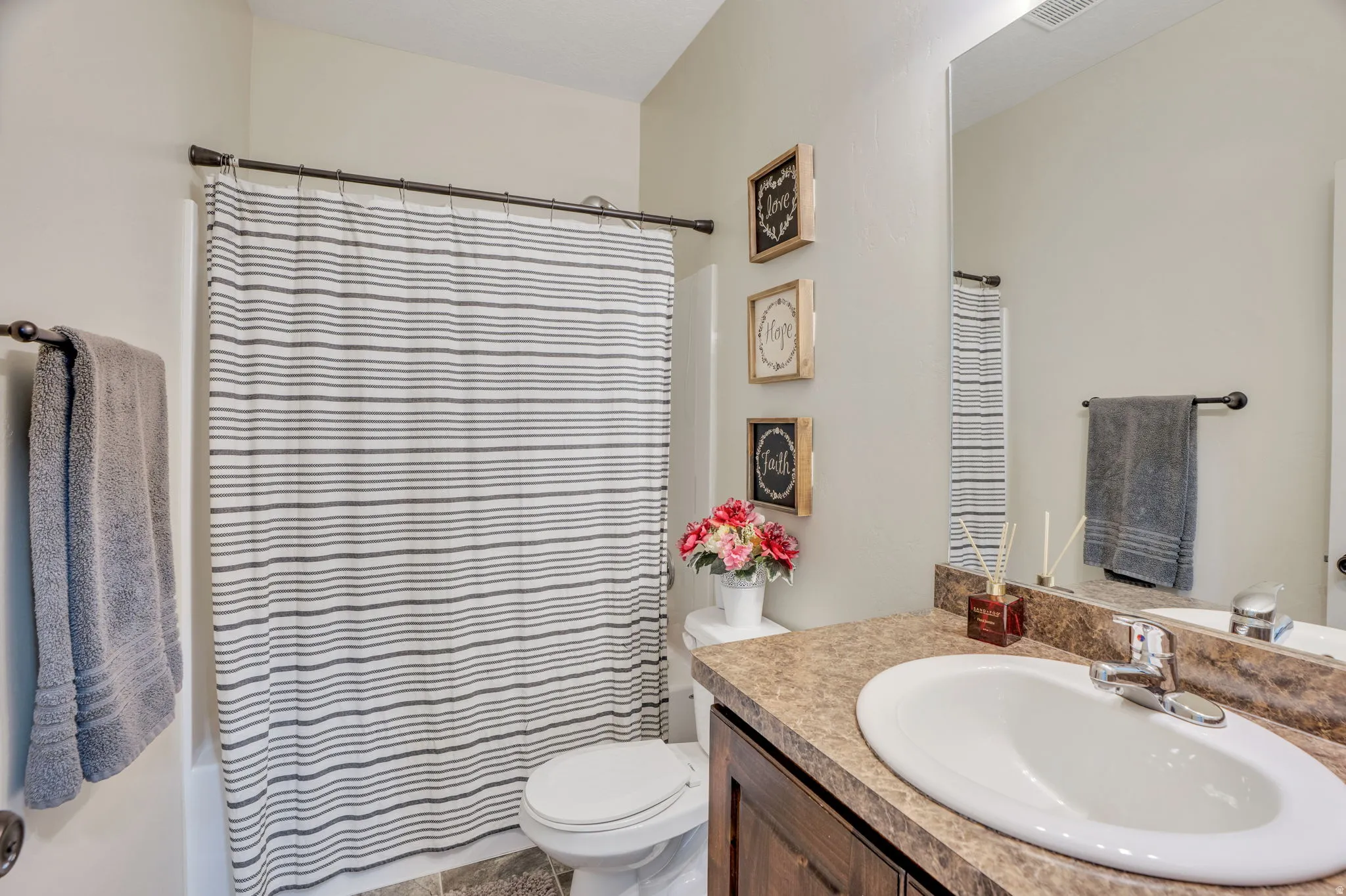 Full vanity mirror, integrated sink, wood-finish cabinetry, and a full bathtub with shower