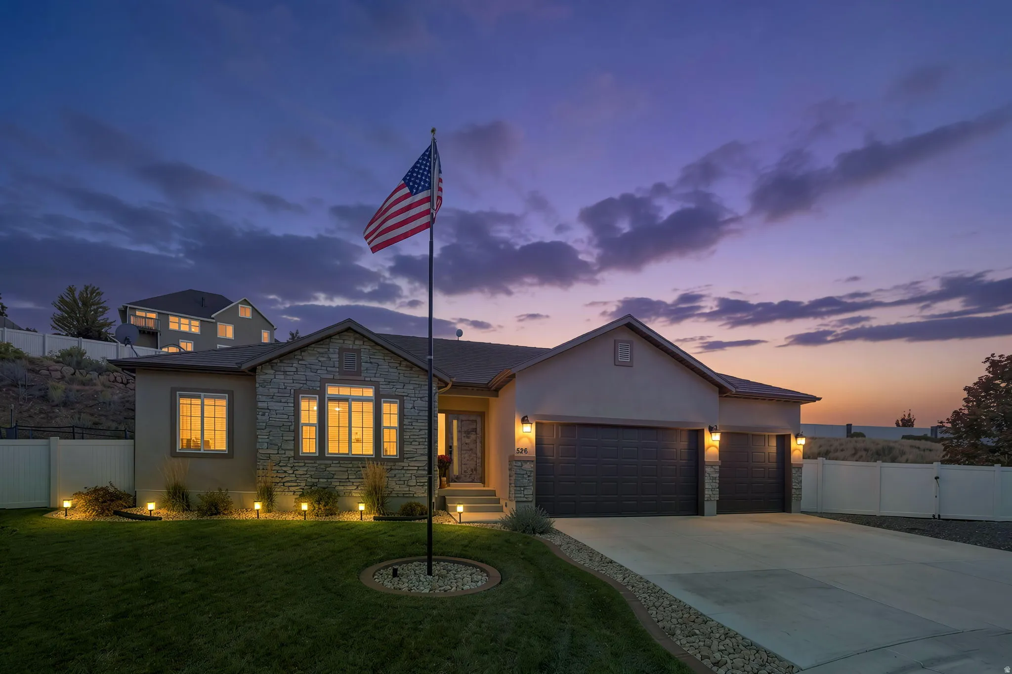 Stucco exterior with stone accents, illuminated landscaping, and a multi-car driveway
