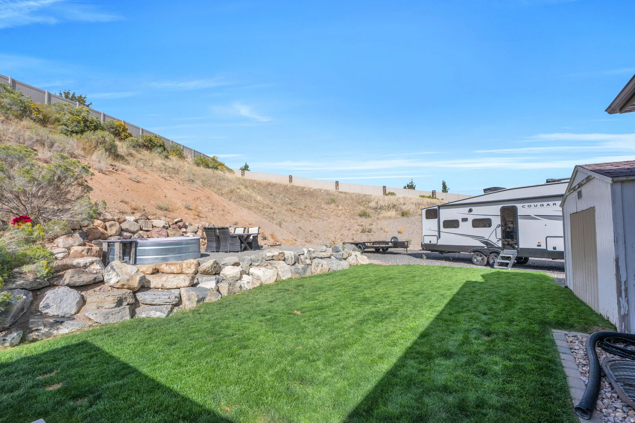 Expansive outdoor space featuring a manicured lawn, stone retaining walls, and a dedicated gravel area