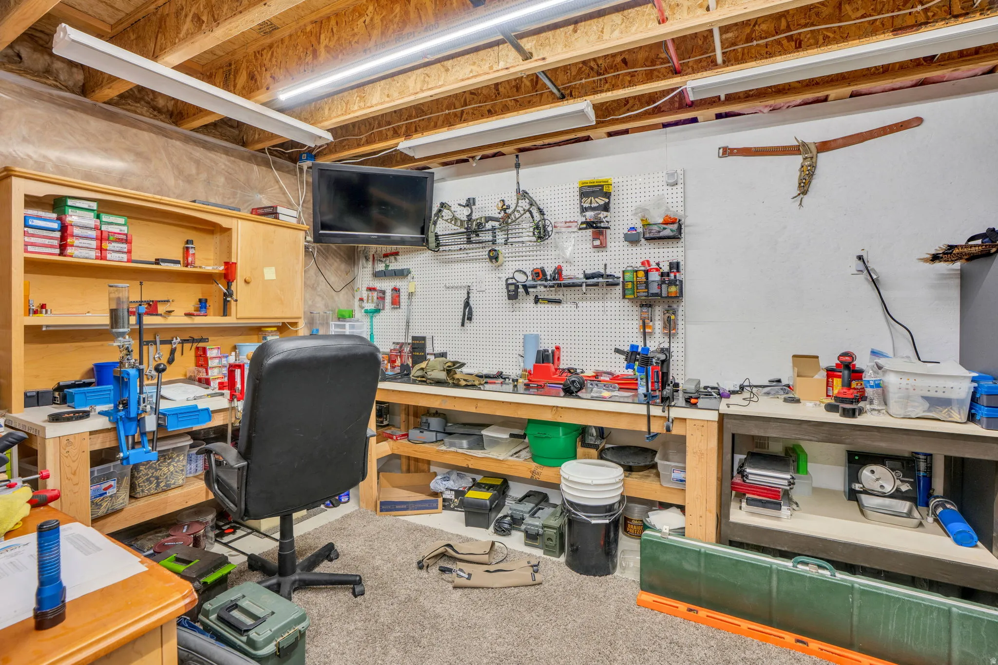 Exposed wood ceiling joists, overhead fluorescent lighting, built-in wooden workbench, built-in wooden shelving unit, white pegboard wall