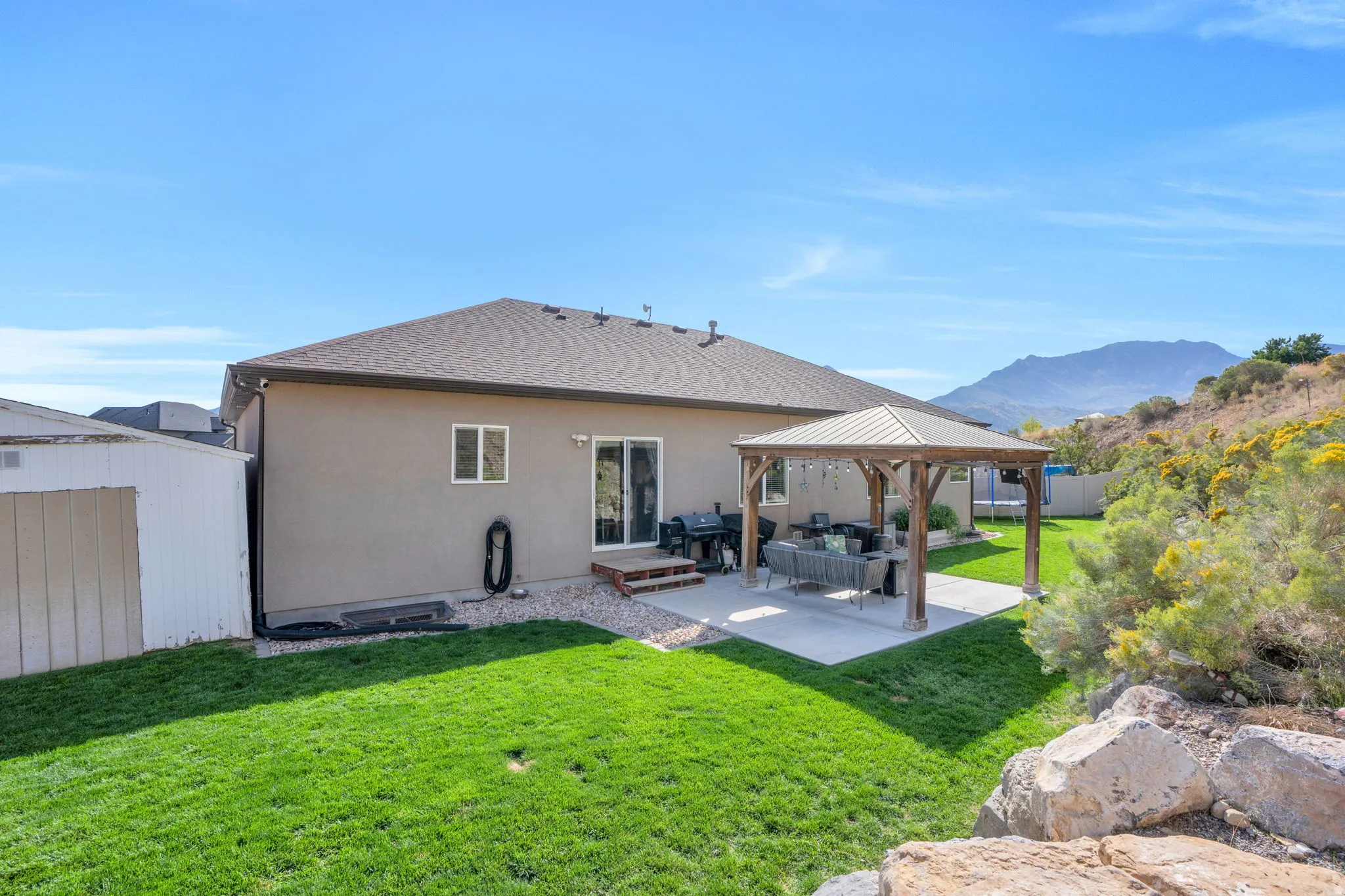 Expansive backyard featuring a manicured lawn, a concrete patio, and a wood-frame gazebo with a metal roof