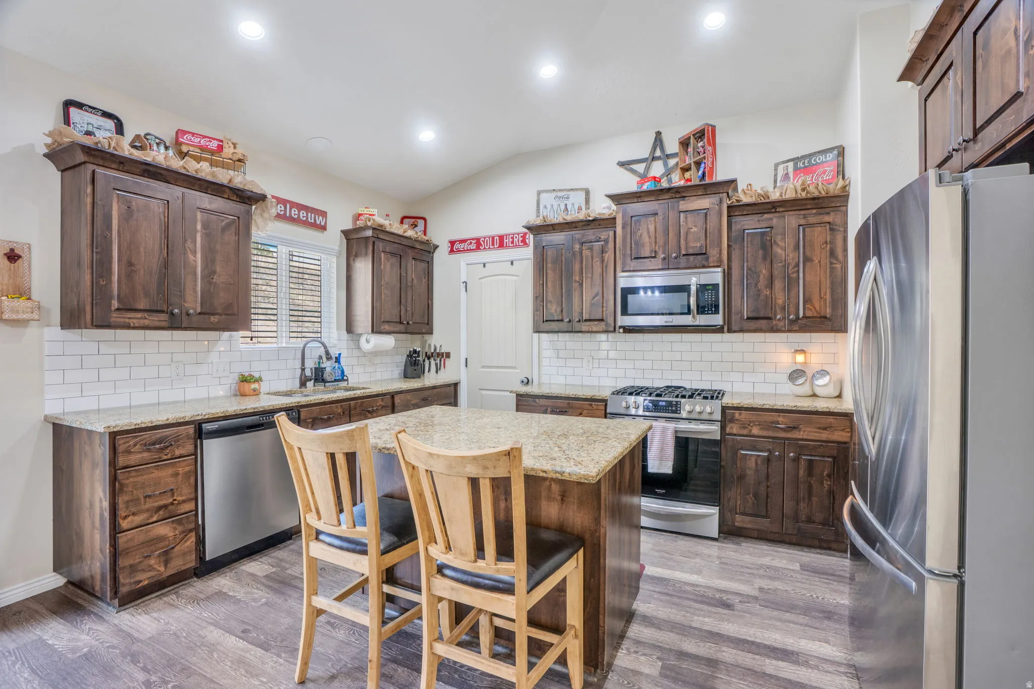 Kitchen featuring wood-finish flooring, dark wood cabinetry, light speckled countertops, a white subway tile backsplash, and stainless steel appliances