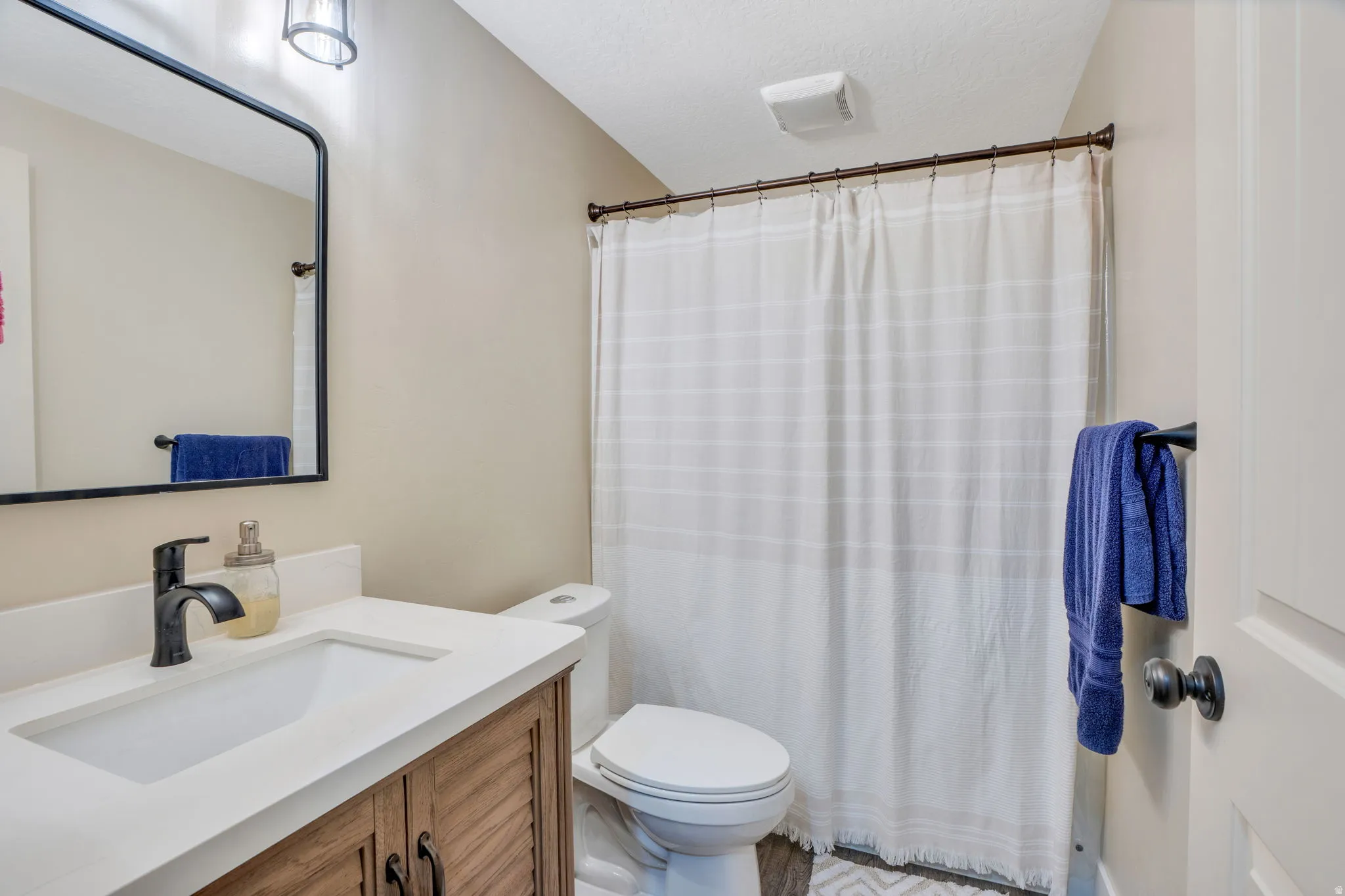 Wood-finish vanity with a white countertop and undermount sink, framed mirror, and a bronze-finish faucet