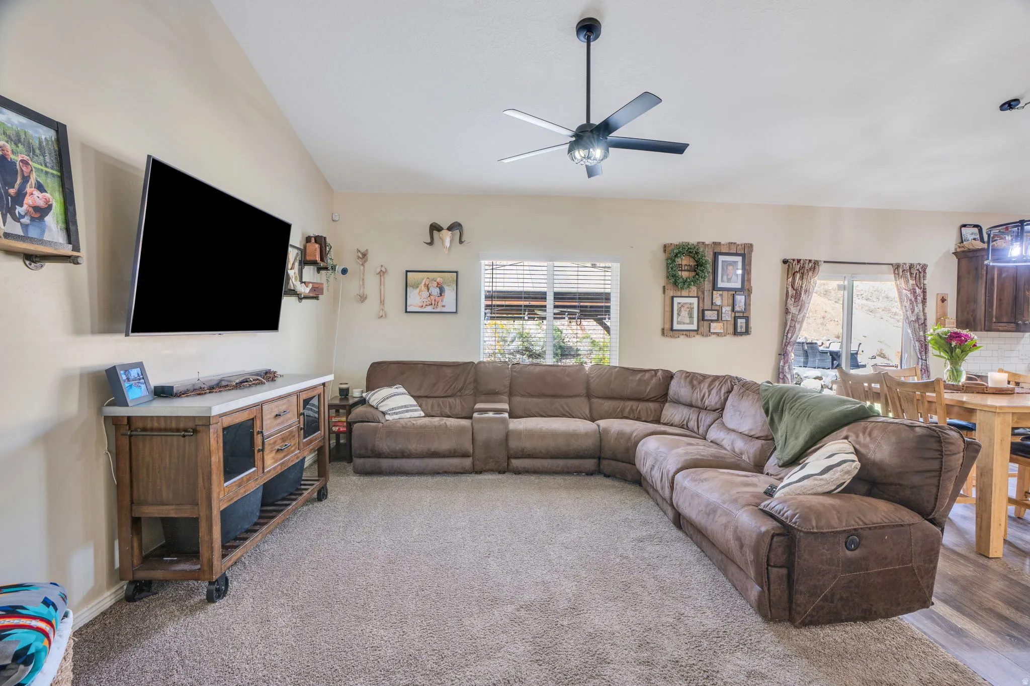 Spacious living area featuring a ceiling fan, wall-mounted television, and light-colored carpeting
