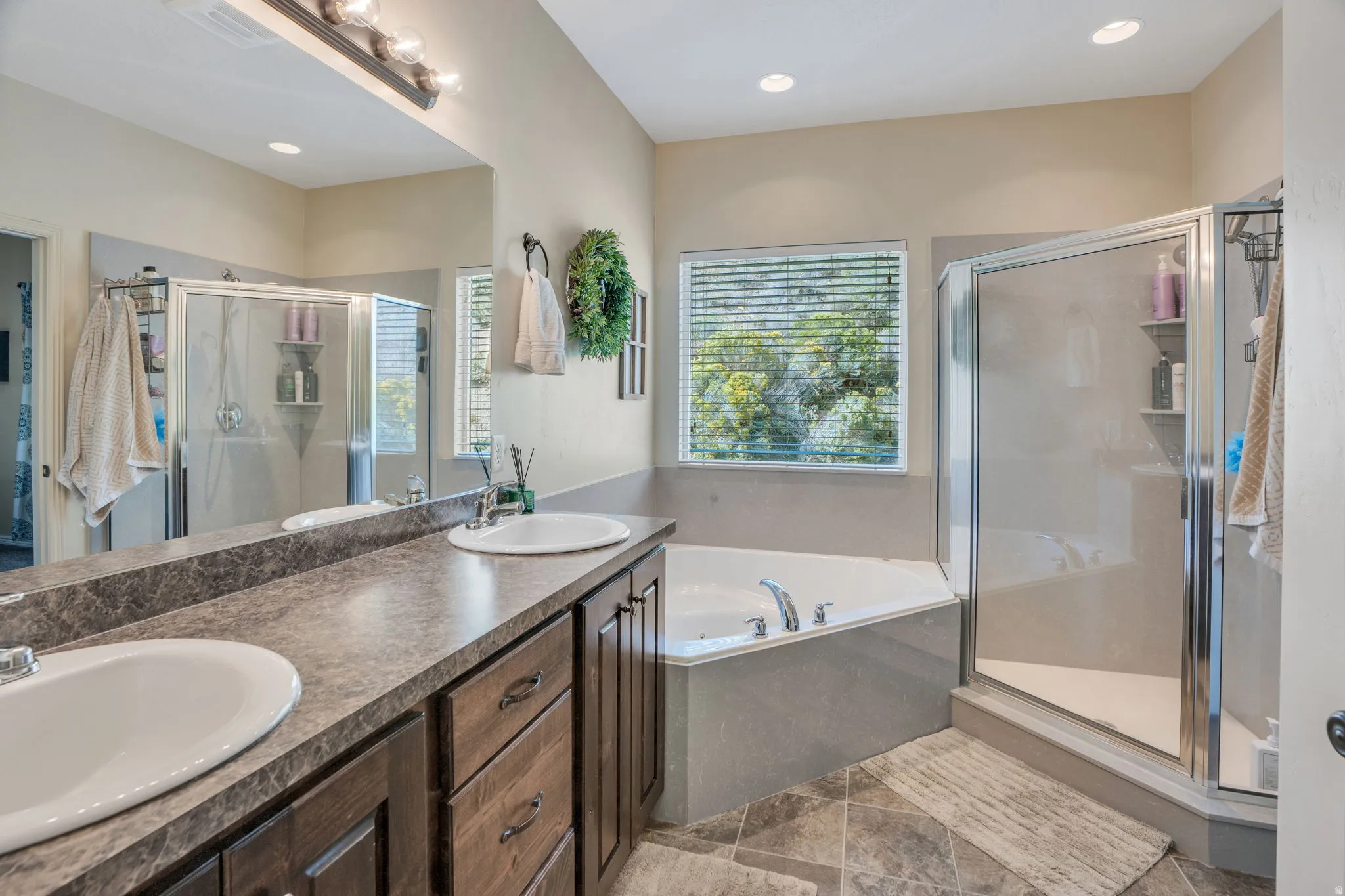 Dual vanity with integrated sinks, wood-finish cabinetry, built-in soaking tub, and glass-enclosed shower