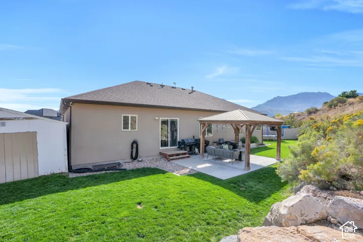 Expansive backyard featuring a manicured lawn, a concrete patio, and a wood-frame gazebo with a metal roof