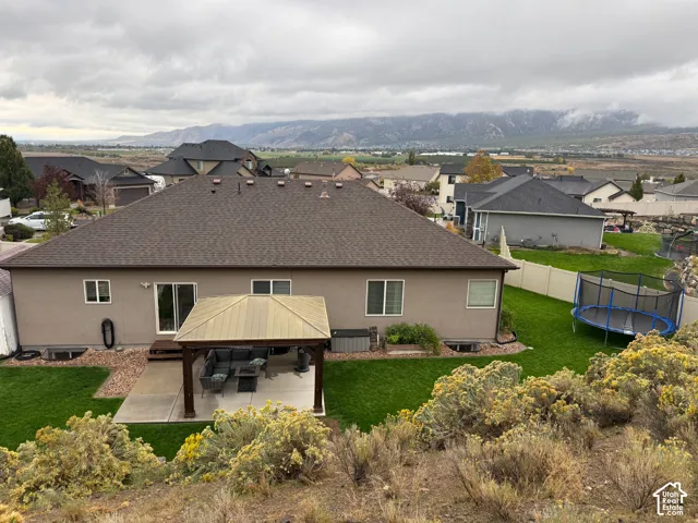 Rear exterior featuring a covered patio with a metal gazebo, a sprawling lawn, and mountain scenery