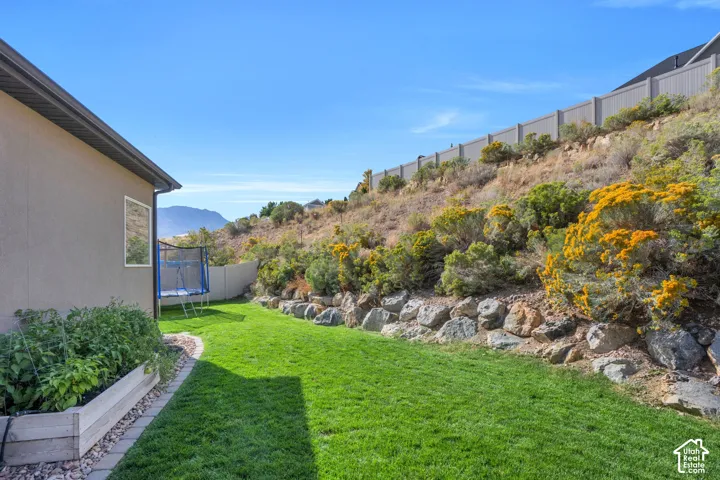 Manicured lawn with a retaining rock wall, adjacent to a sloped, natural landscape