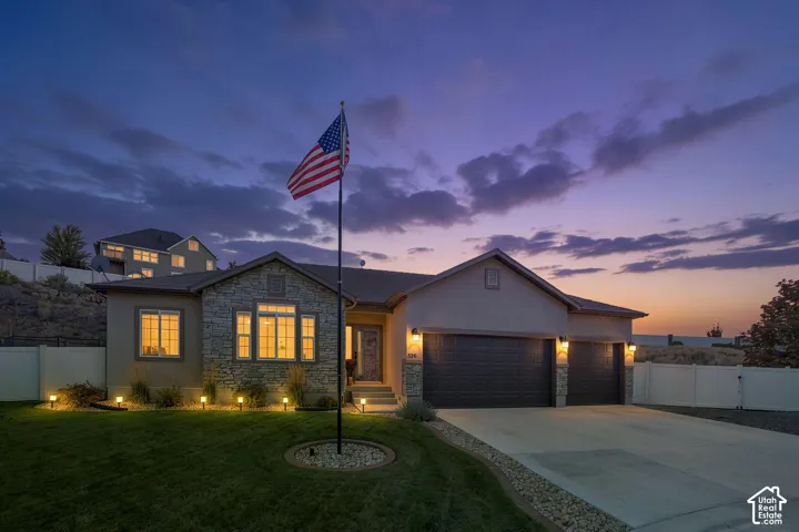 Stucco exterior with stone accents, illuminated landscaping, and a multi-car driveway