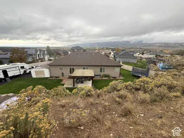Rear exterior featuring a covered patio, manicured lawn, metal storage shed, and mountainous backdrop