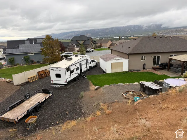 Backyard area featuring a lawn, gravel parking space, detached storage shed, and a covered patio structure, all set against a mountain backdrop