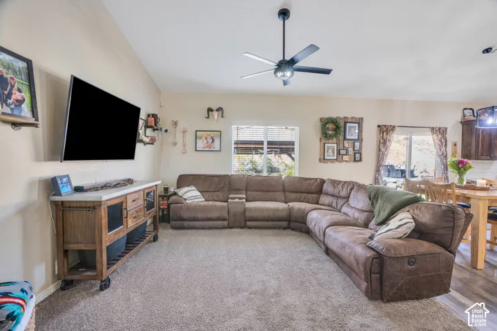 Spacious living area featuring a ceiling fan, wall-mounted television, and light-colored carpeting