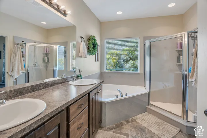 Dual vanity with integrated sinks, wood-finish cabinetry, built-in soaking tub, and glass-enclosed shower