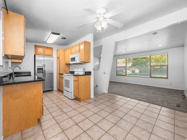 Kitchen with wood cabinetry, dark countertops, tile flooring, and stainless steel refrigerator