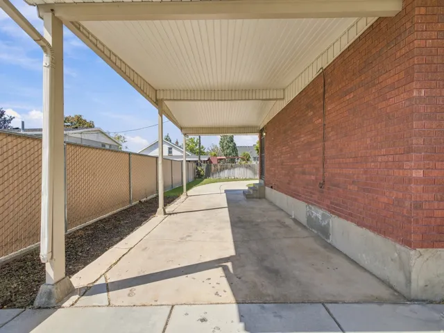 Covered concrete walkway featuring a brick exterior wall and chain-link fencing