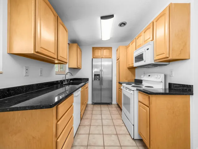 Kitchen featuring wood cabinetry, black countertops, tile flooring, and stainless steel refrigerator