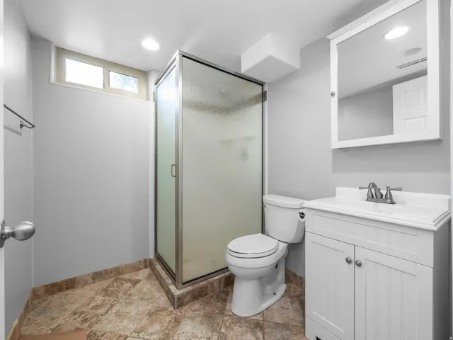 Bathroom featuring a stand-up shower with a frosted glass enclosure, white vanity with integrated sink, wall-mounted medicine cabinet, and tiled flooring