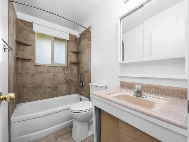 Built-in bathtub with a tile surround, window with privacy glass, integrated shelving, and a vanity with a countertop sink