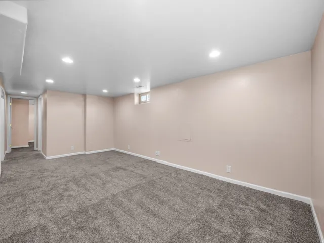 Recessed lighting, neutral wall tones, gray carpeting, and a small casement window