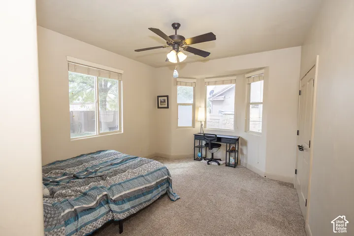 Recessed bay window, ceiling fan, neutral wall color, light-colored carpet, and solid panel door