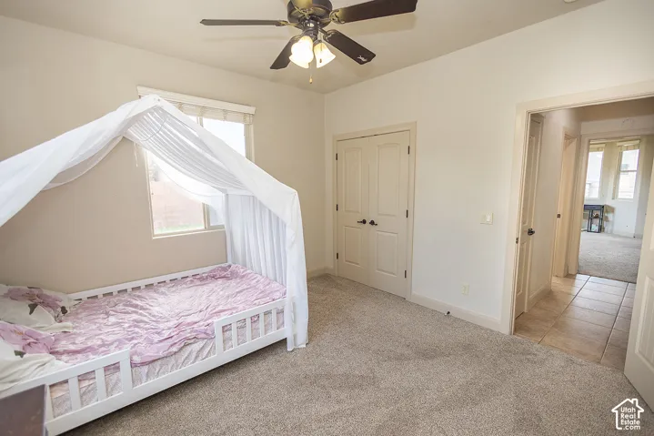 Neutral wall color, ceiling fan with integrated lighting, window with window treatment, light-toned carpet flooring, and double-door closet