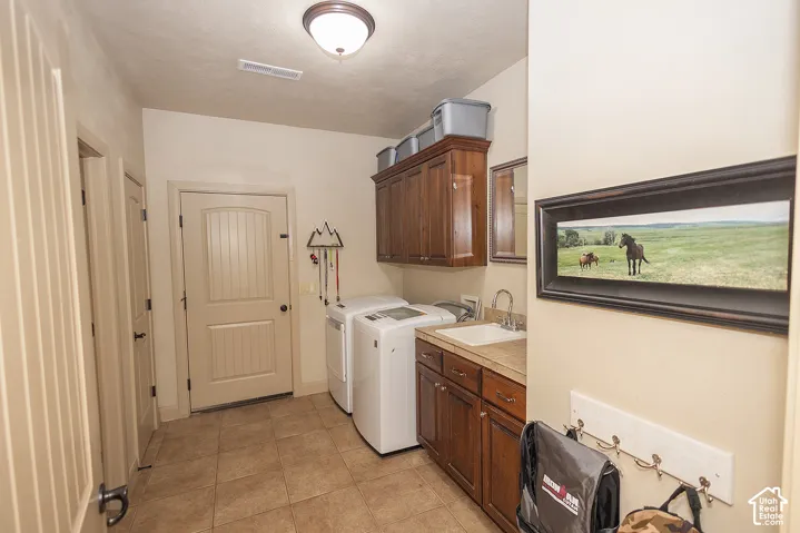 Laundry area featuring tiled flooring, wood-finish cabinetry, a utility sink with a chrome faucet, and a built-in overhead light fixture